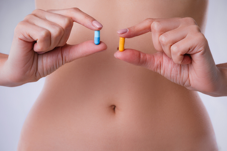 Pills with probiotics on the background of the female abdomen.